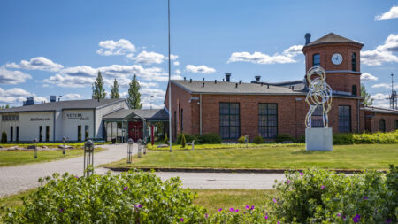 Salon Taidemuseo Veturitallin julkisivu ja sen pihamaata aurikoisena kesäpäivänä. Veturitallin edustalla seisoo korkea veistos.