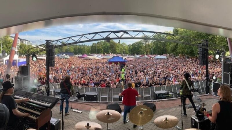 Yhtye esiintymässä Salon Iltatorin lavalla. Lavan edessä ja koko torilla on paljon kuuntelijoita.